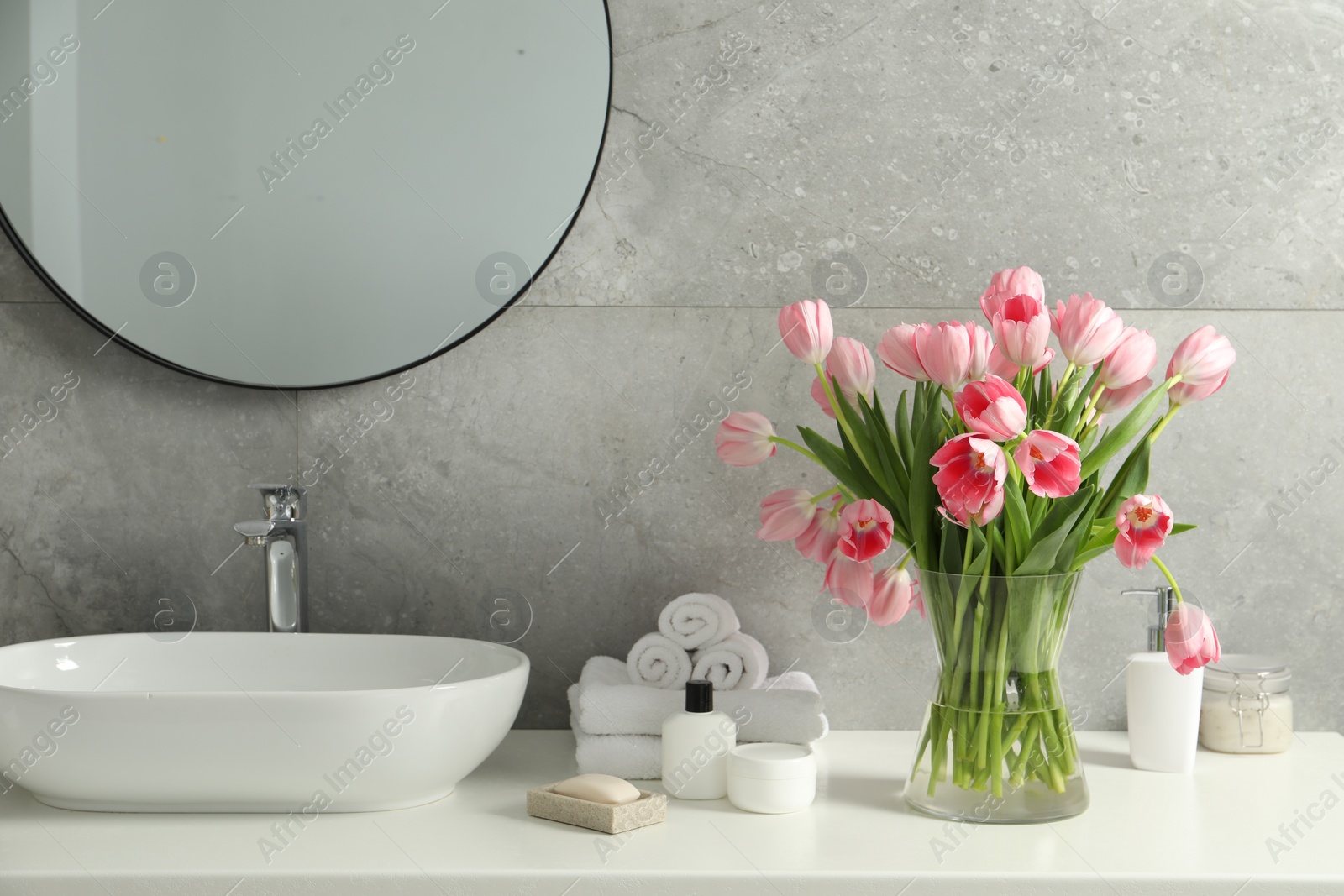 Photo of Vase with beautiful pink tulips and toiletries near sink in bathroom