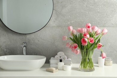 Photo of Vase with beautiful pink tulips and toiletries near sink in bathroom