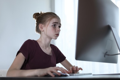 Photo of Upset teenage girl using computer at table indoors. Danger of internet