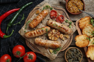 Tasty fresh grilled sausages with vegetables on wooden table, flat lay