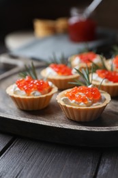 Photo of Delicious tartlets with red caviar and cream cheese served on wooden table, closeup