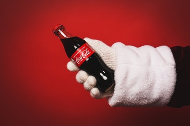Photo of MYKOLAIV, UKRAINE - JANUARY 18, 2021: Santa Claus holding Coca-Cola bottle in hand on red background, closeup