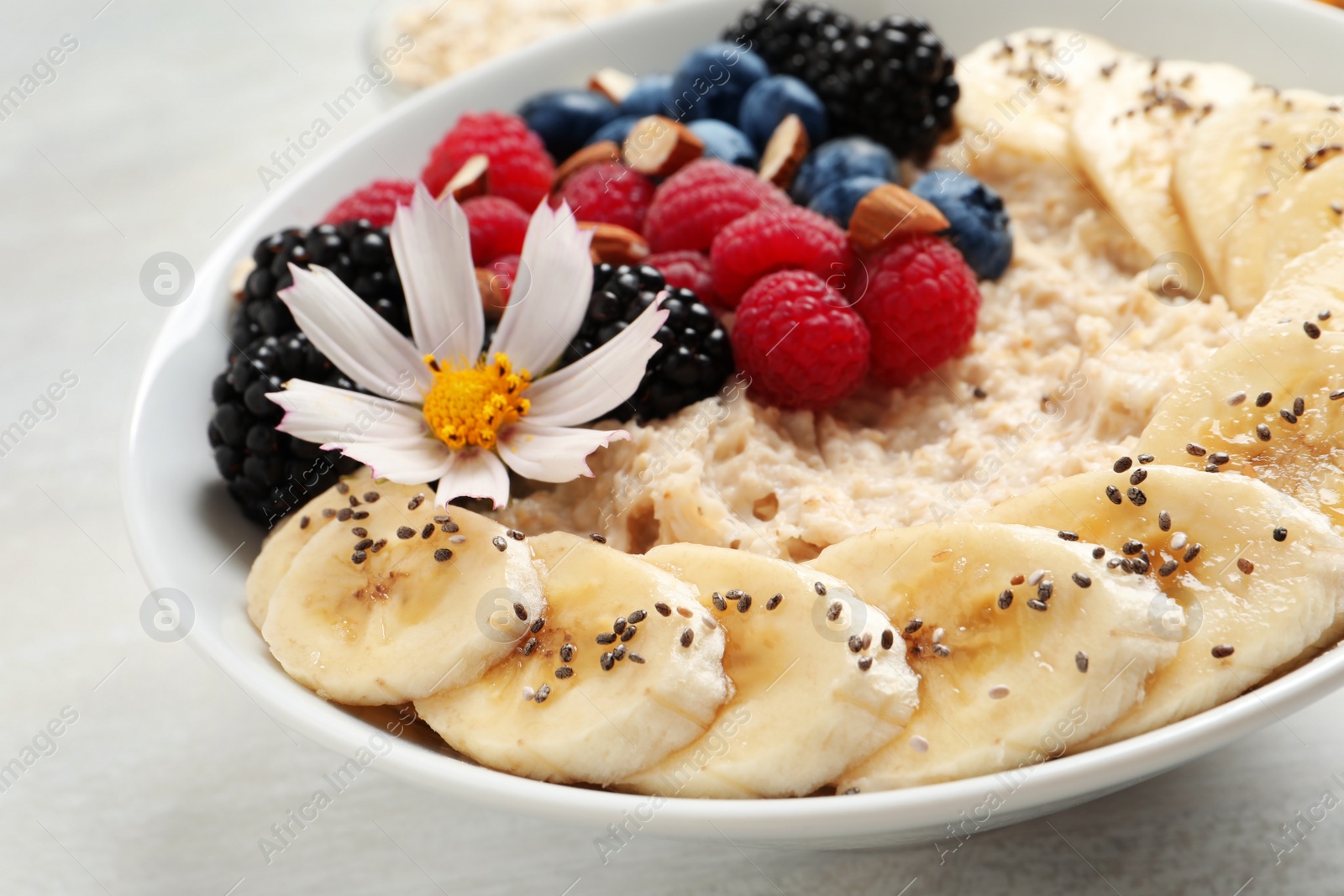 Photo of Tasty oatmeal porridge with berries, banana and chia seeds on light table, closeup