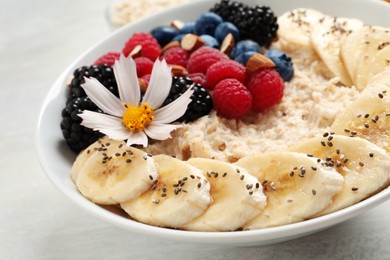Photo of Tasty oatmeal porridge with berries, banana and chia seeds on light table, closeup