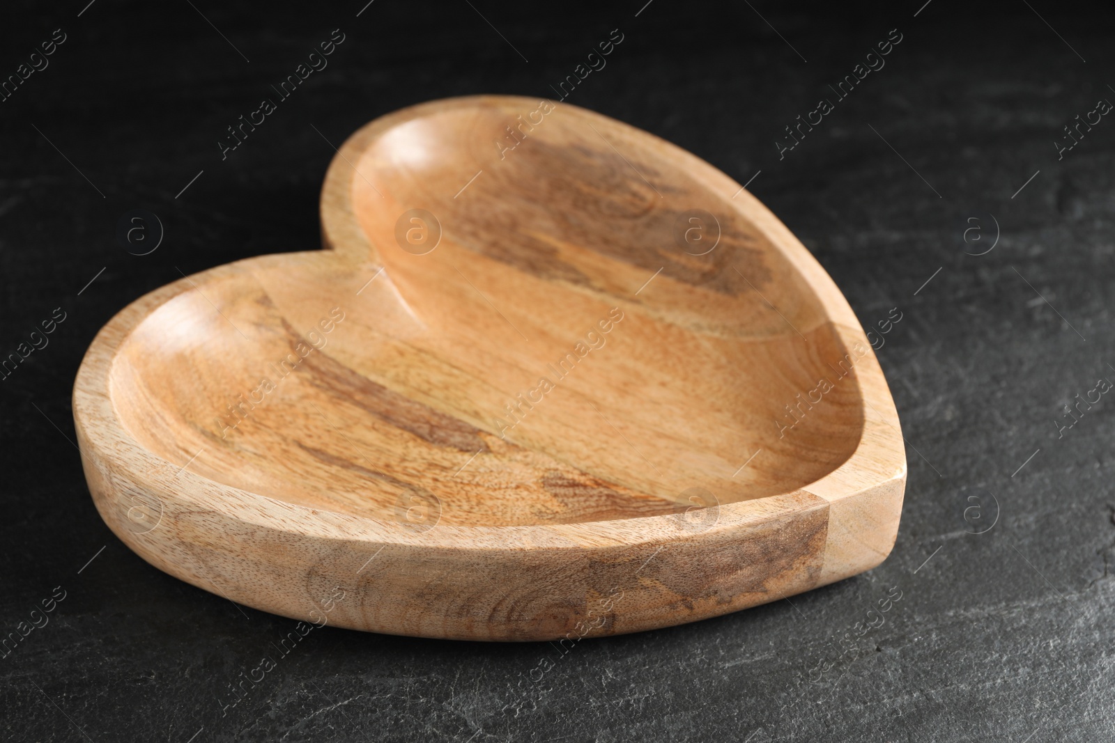 Photo of Empty heart shaped wooden plate on black table, closeup