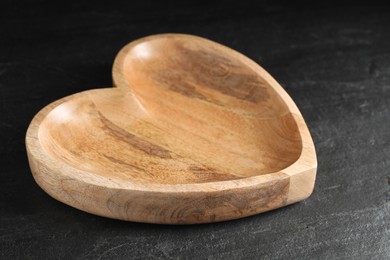 Empty heart shaped wooden plate on black table, closeup