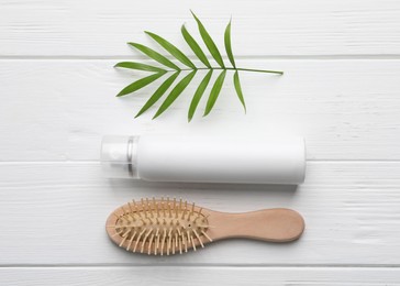 Dry shampoo spray, hairbrush and green twig on white wooden table, flat lay