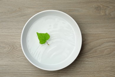 Photo of White bowl with water and green leaf on wooden table, top view