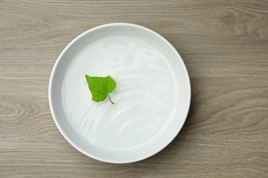 White bowl with water and green leaf on wooden table, top view