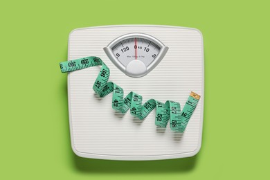 Bathroom scale with measure tape on light green background, top view