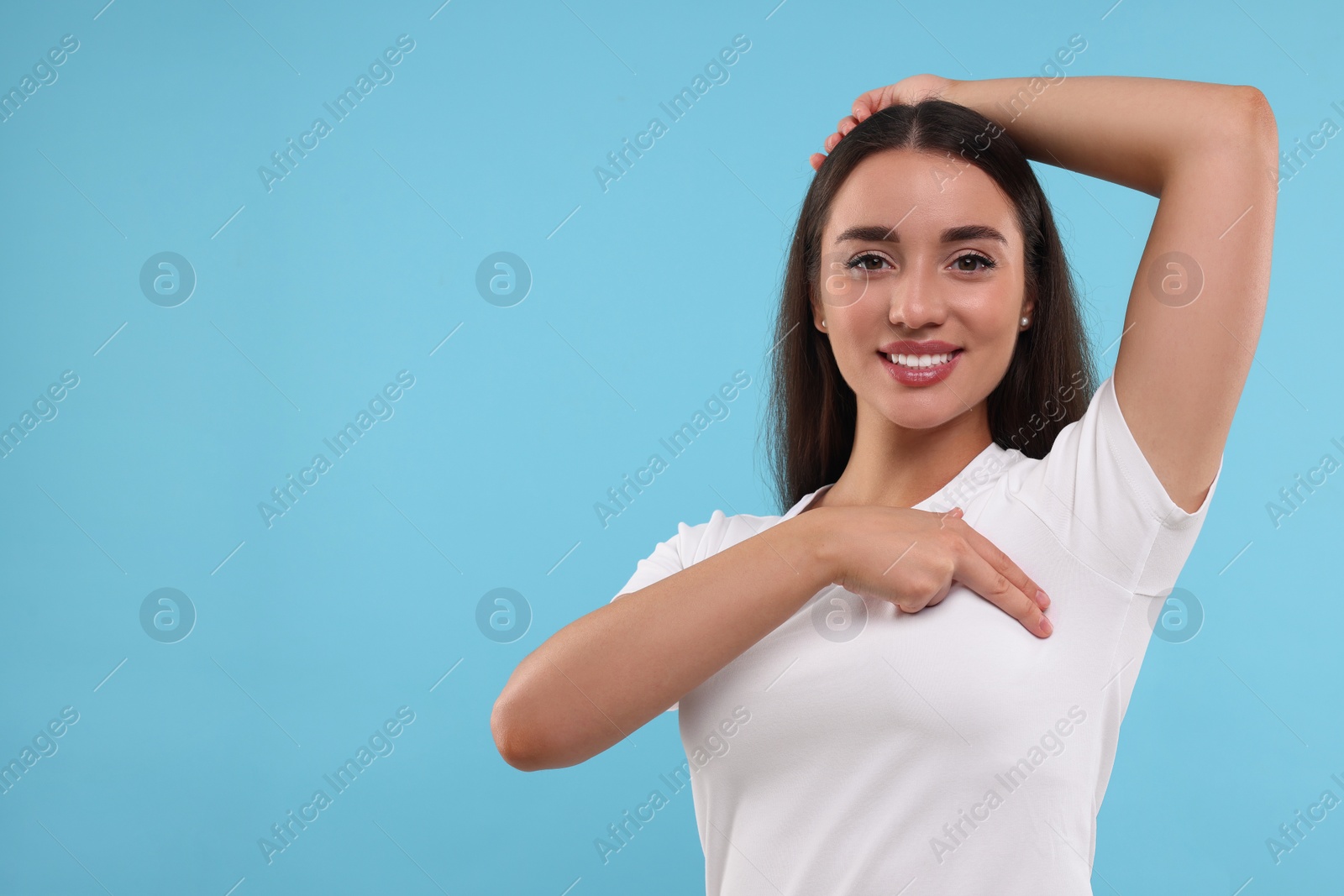 Photo of Beautiful happy woman doing breast self-examination on light blue background, space for text