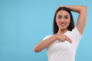 Beautiful happy woman doing breast self-examination on light blue background, space for text