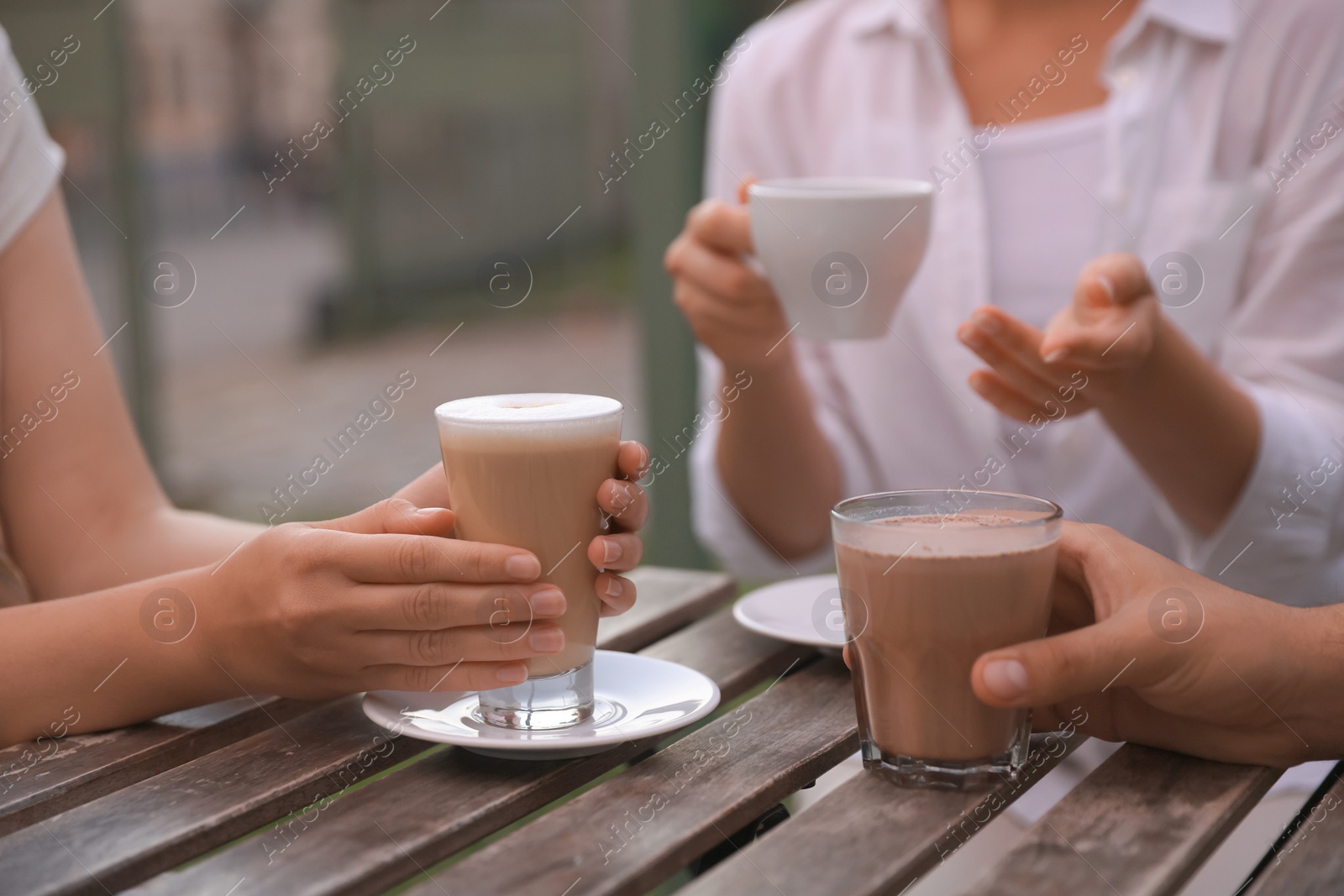 Photo of Friends drinking coffee and cocoa at wooden table in outdoor cafe, closeup