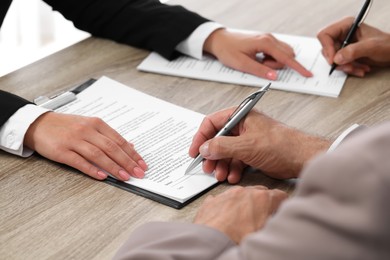 Photo of Manager showing client where he must to mark signature at light wooden table indoors, closeup