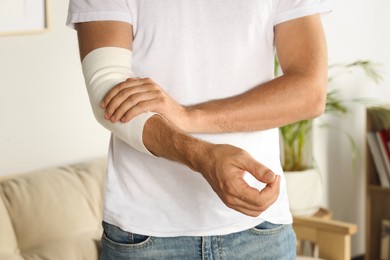 Photo of Man with arm wrapped in medical bandage indoors, closeup