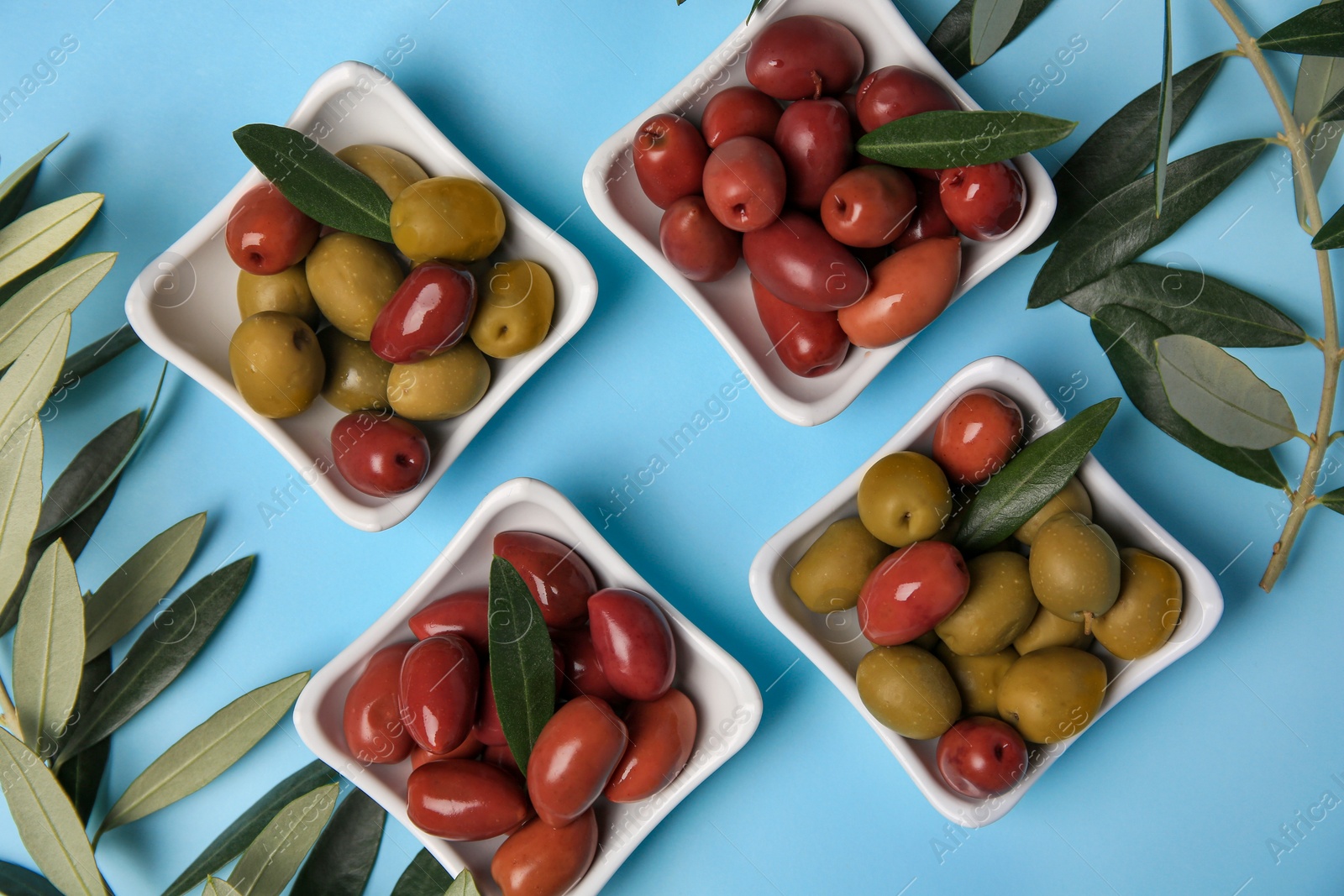 Photo of Different fresh olives and green leaves on light blue background, flat lay