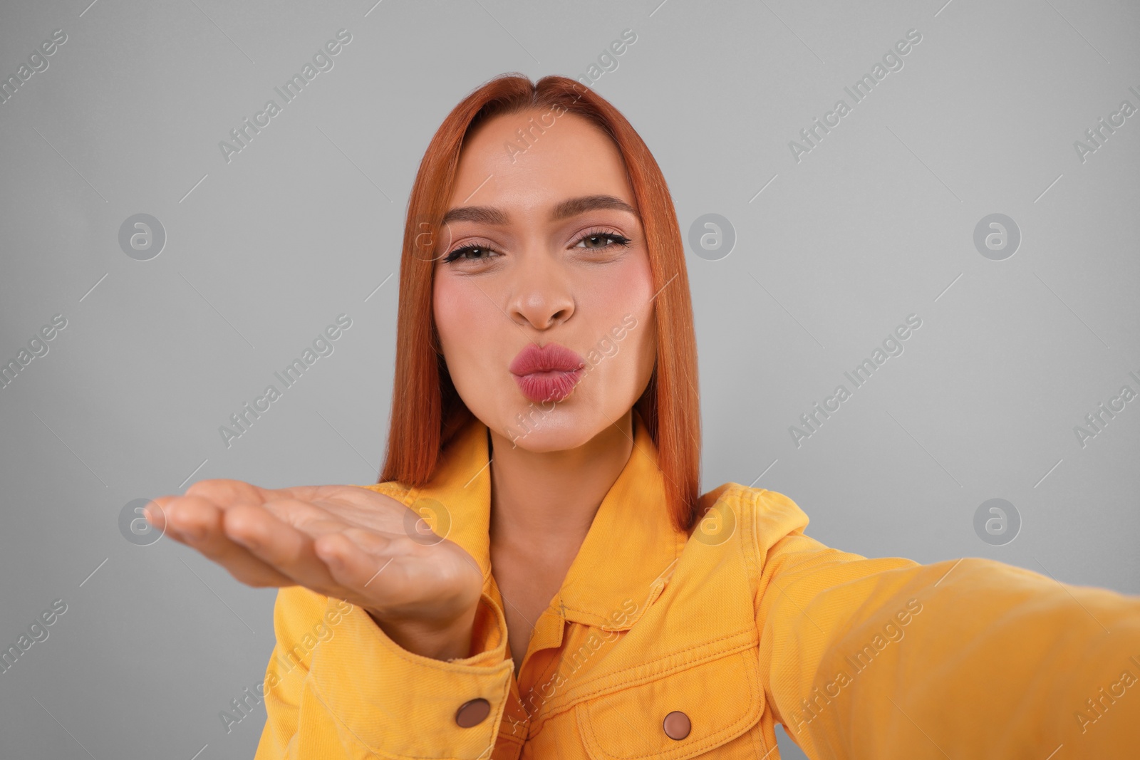 Photo of Beautiful woman taking selfie and blowing kiss on light grey background