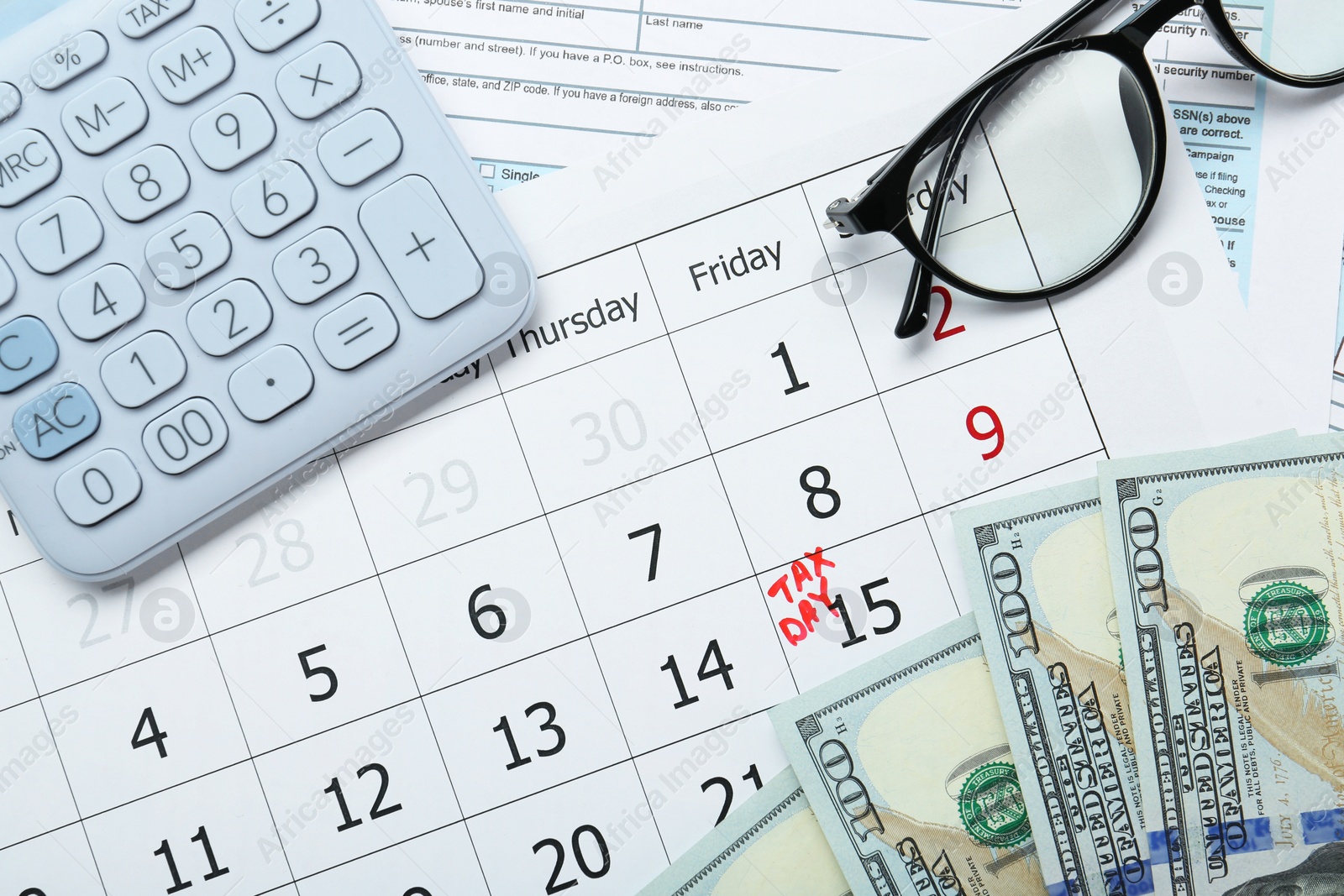 Photo of Calendar with date reminder about tax day, documents, money, calculator and glasses, top view