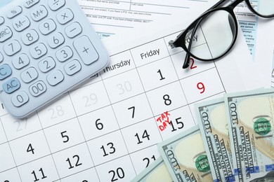 Photo of Calendar with date reminder about tax day, documents, money, calculator and glasses, top view