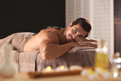 Photo of Handsome young man receiving hot stone massage in spa salon