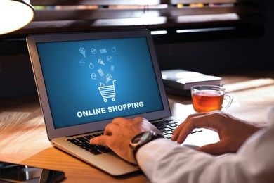 Man using laptop for online shopping at wooden table, closeup