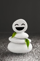 Photo of Stack of stones with drawn happy face and green leaves on grey background. Zen concept