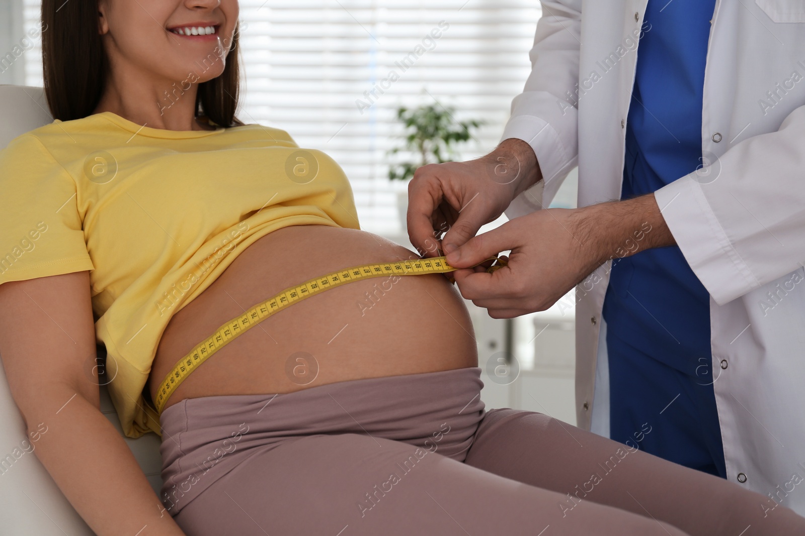 Photo of Doctor measuring pregnant woman's belly with tape in clinic, closeup