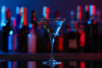 Photo of Martini glass with cocktail and olives on counter in bar