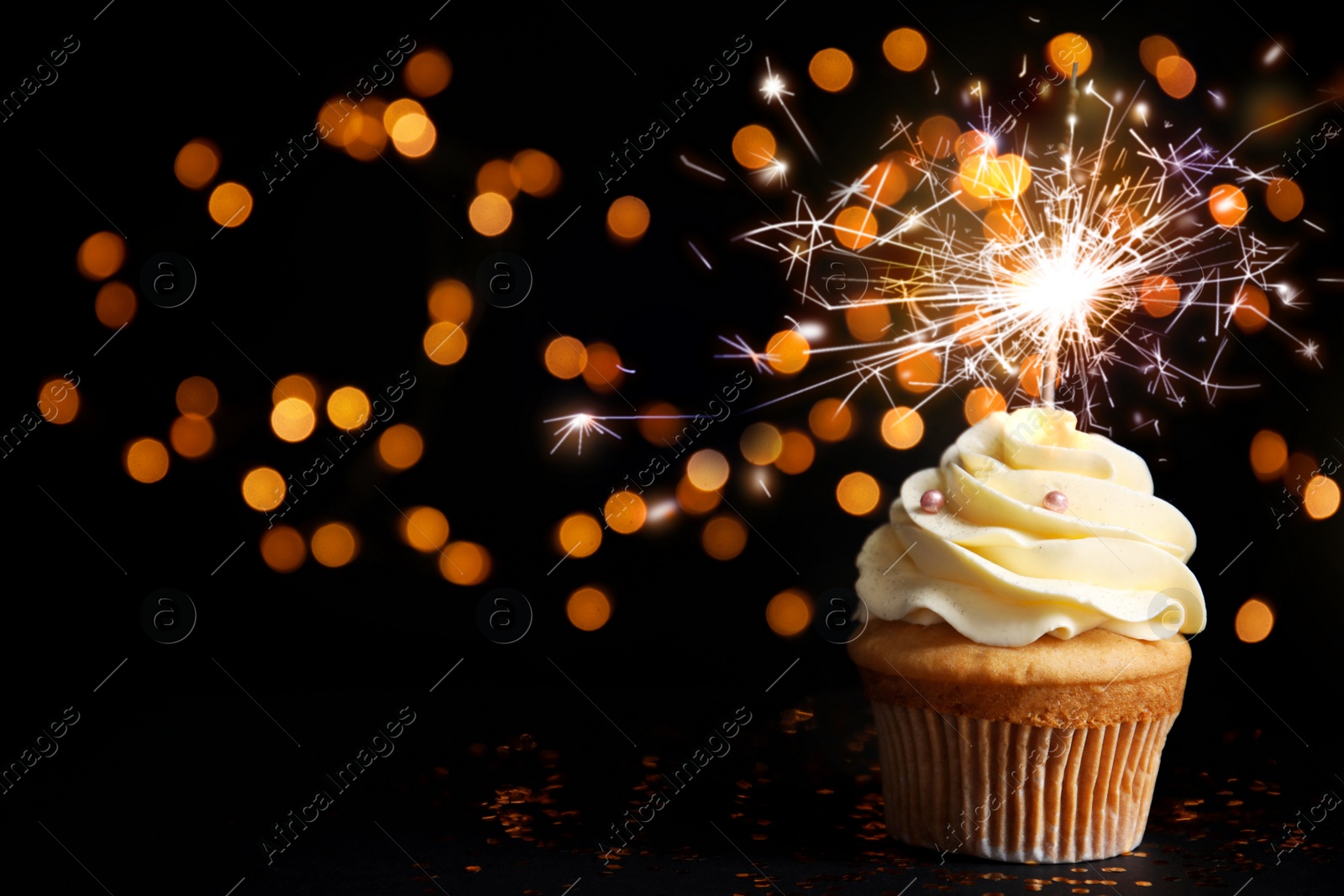 Image of Delicious birthday cupcake with sparkler on black table against blurred lights. Space for text