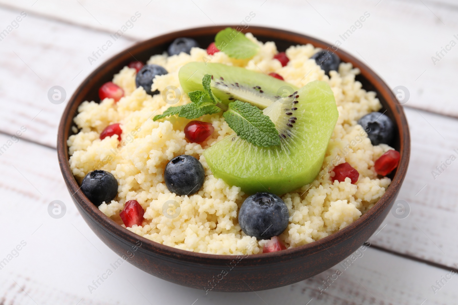 Photo of Bowl of tasty couscous with kiwi, blueberries and pomegranate on white table, closeup