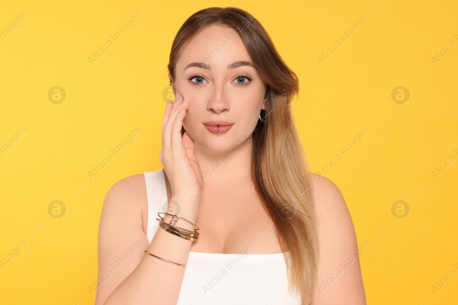 Photo of Young woman with lip and ear piercings on yellow background