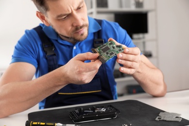 Photo of Male technician repairing hard drive at table indoors