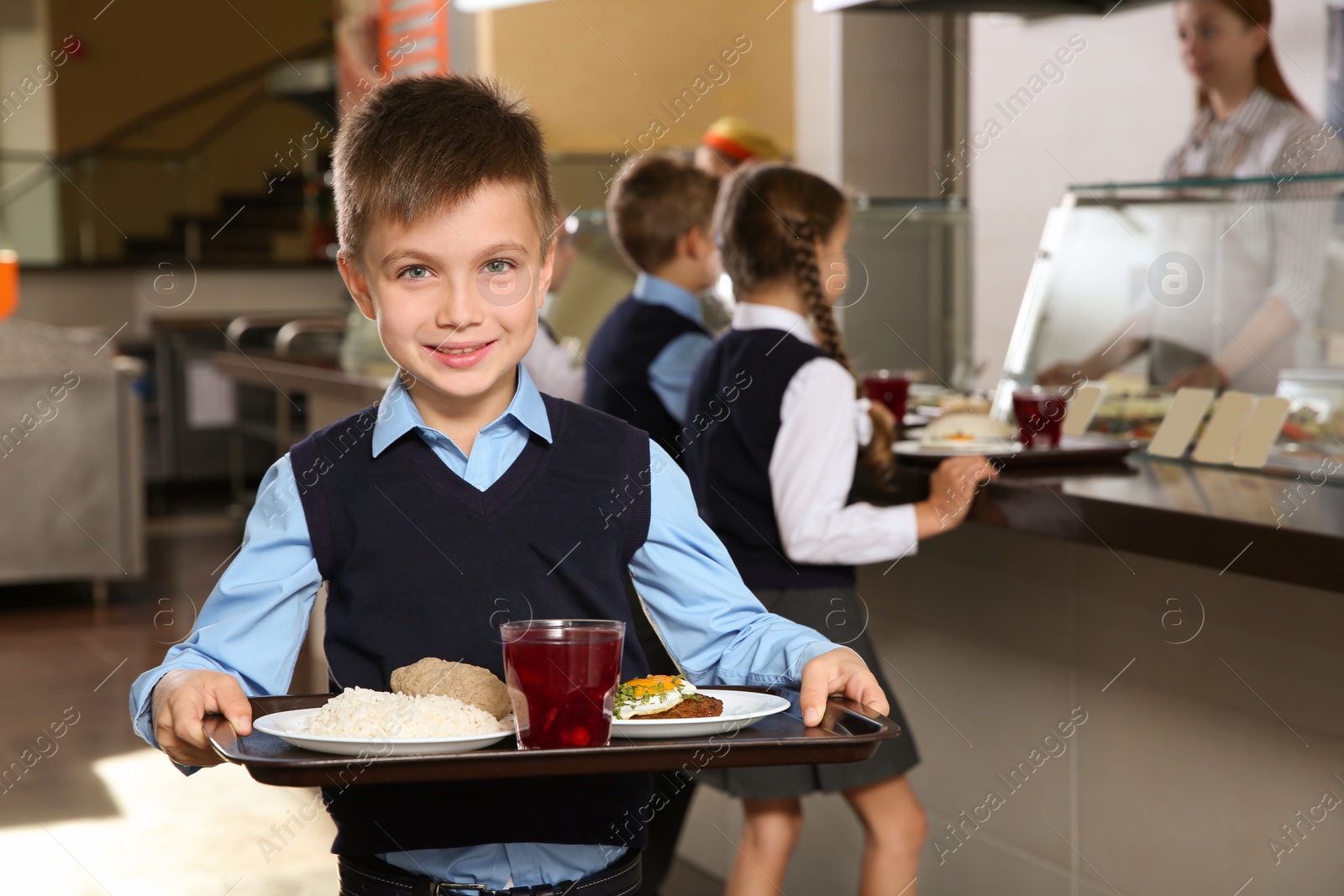 Photo of Cute boy holding tray with healthy food in school canteen