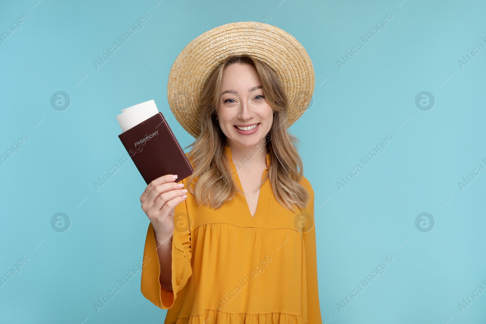 Photo of Happy young woman with passport, ticket and hat on light blue background