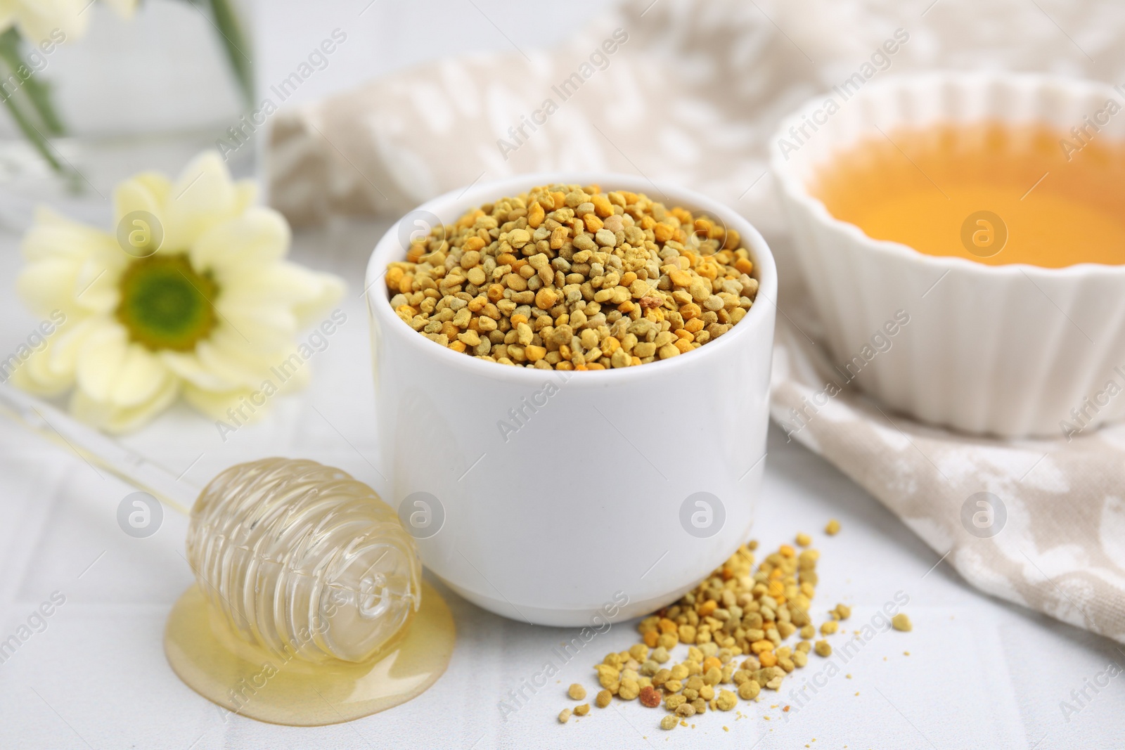 Photo of Fresh bee pollen granules and dipper with honey on white table, closeup