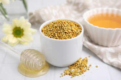 Fresh bee pollen granules and dipper with honey on white table, closeup