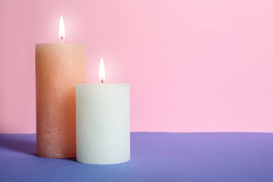 Decorative wax candles on table against color background