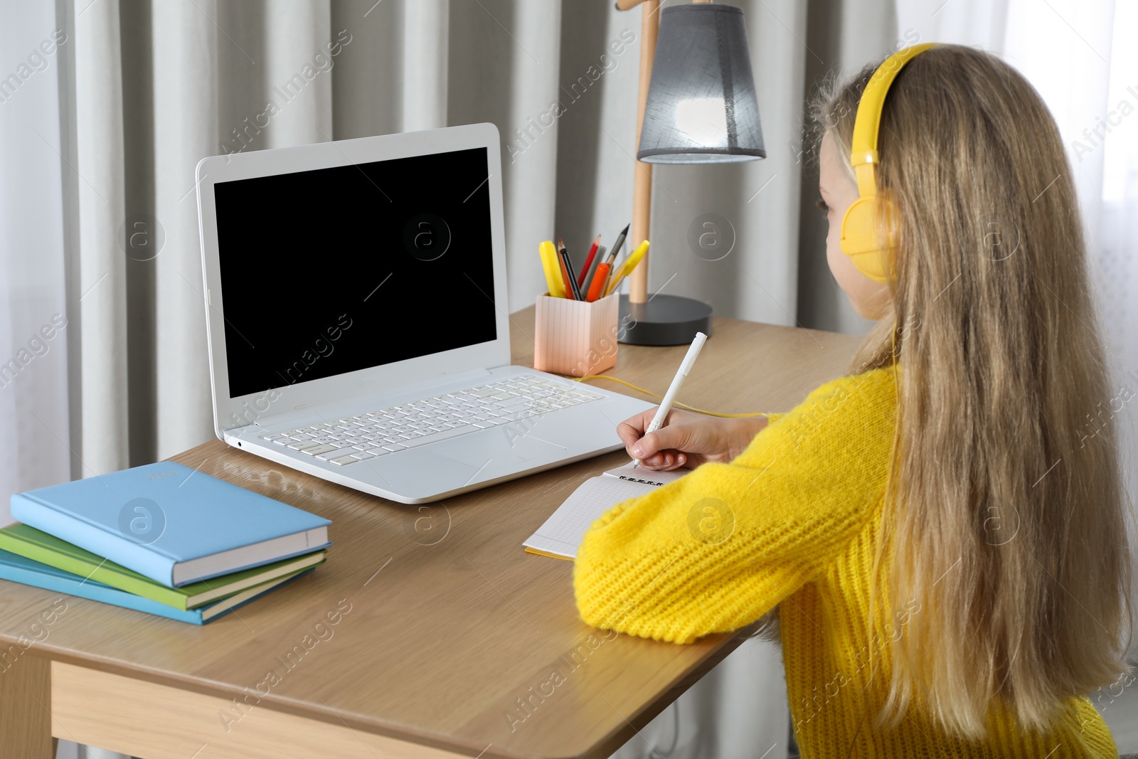 Photo of Cute little girl with modern laptop studying online at home. E-learning