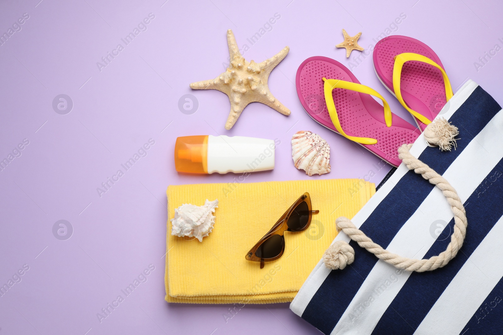 Photo of Stylish bag with beach accessories on violet background, flat lay. Space for text