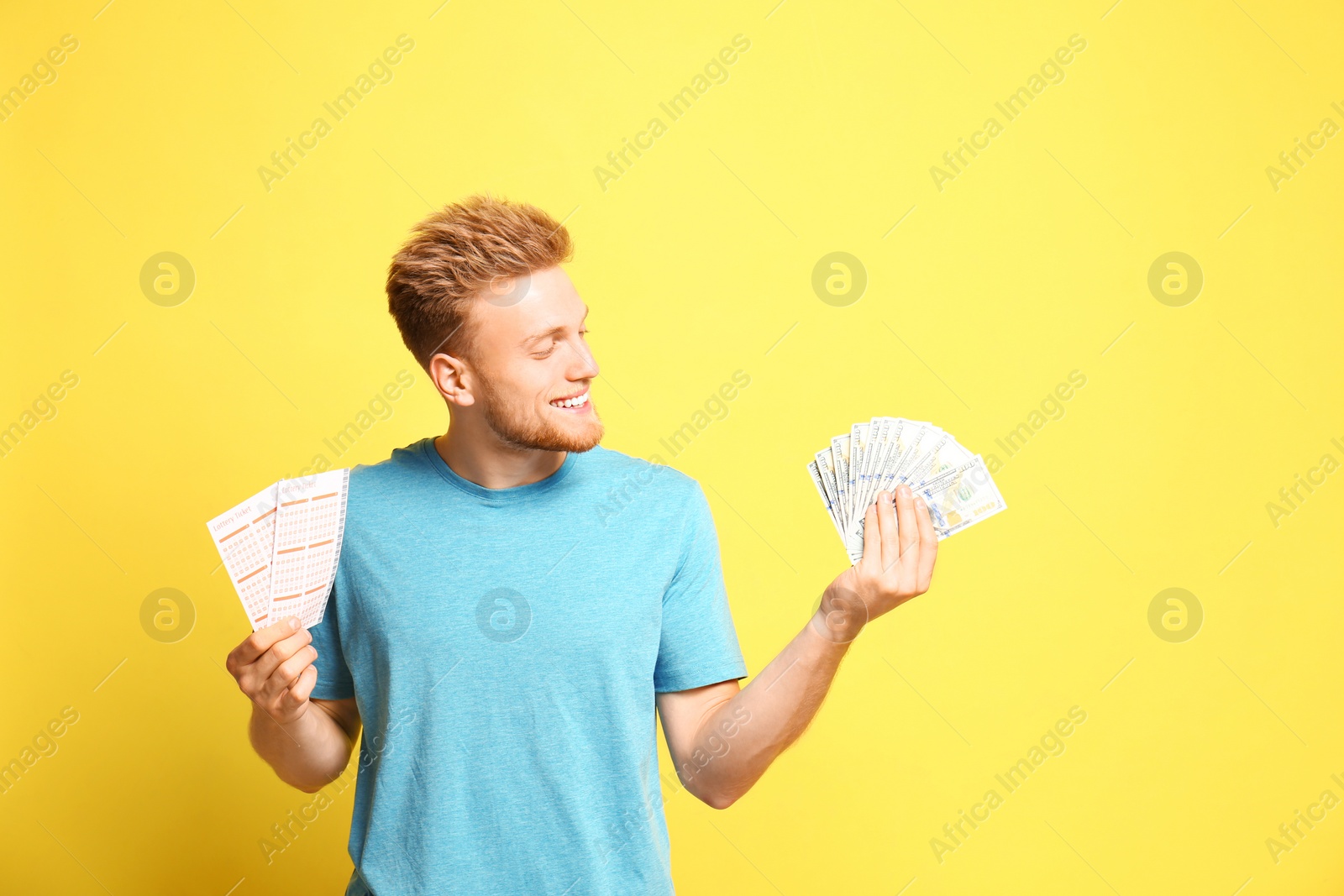 Photo of Portrait of happy young man with money and lottery tickets on yellow background