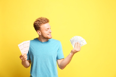 Portrait of happy young man with money and lottery tickets on yellow background