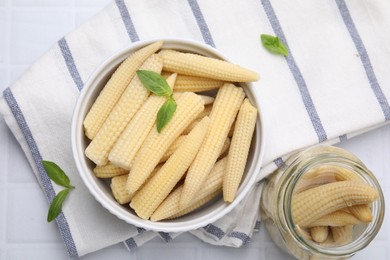 Canned baby corns with basil on white tiled table, flat lay