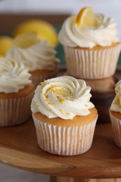 Delicious lemon cupcakes with white cream on wooden stand, closeup