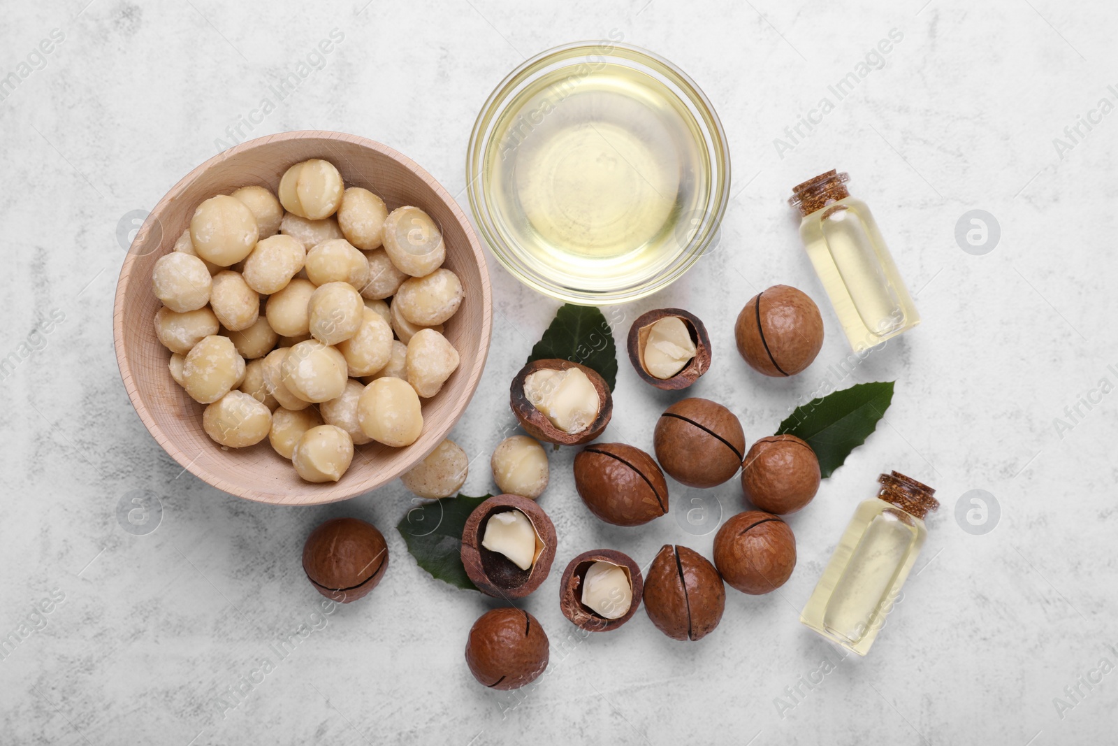 Photo of Delicious organic Macadamia nuts and cosmetic oil on light gray table, flat lay