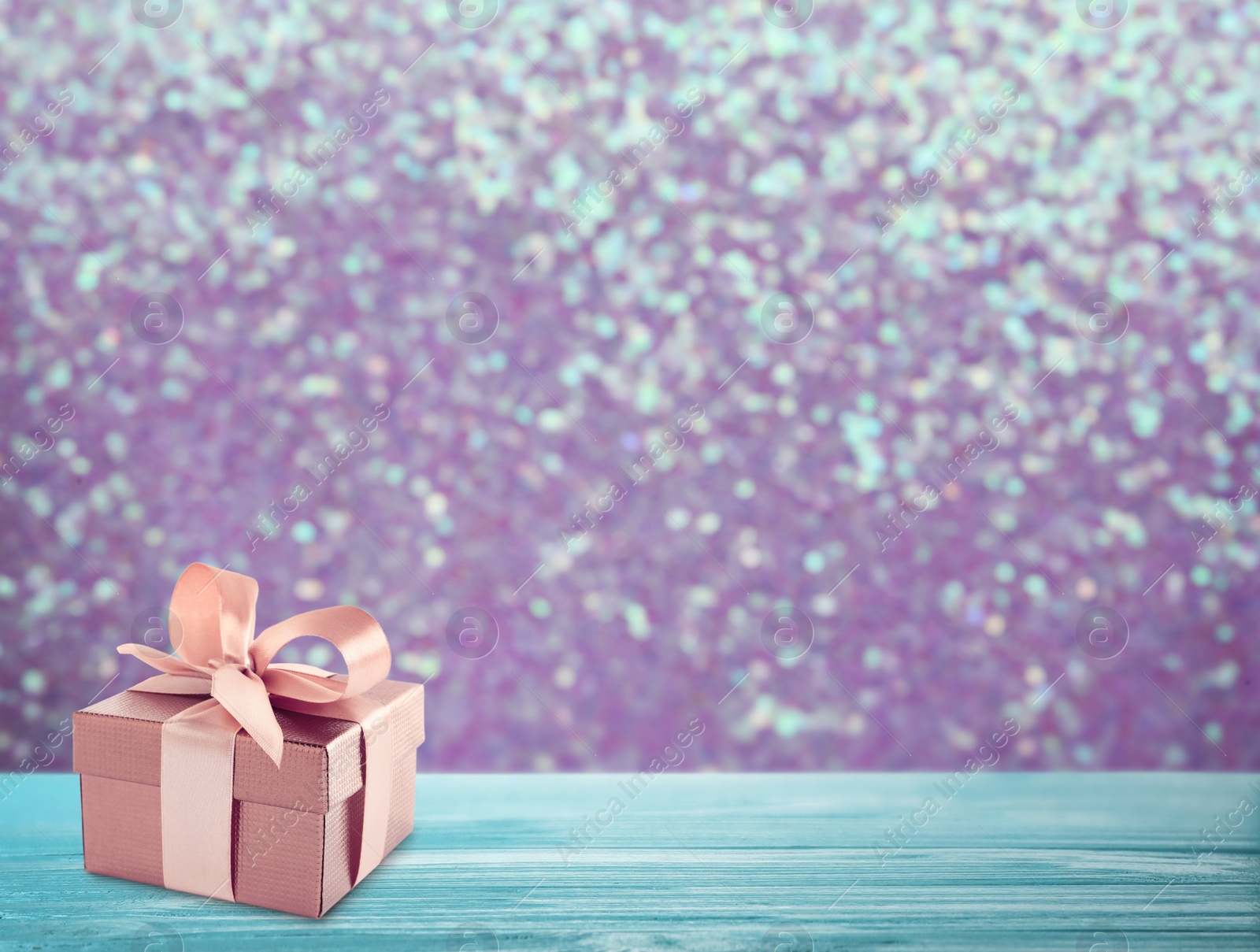 Image of Beautiful gift box on blue wooden table against shiny color background, bokeh effect. Space for text