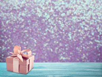 Beautiful gift box on blue wooden table against shiny color background, bokeh effect. Space for text