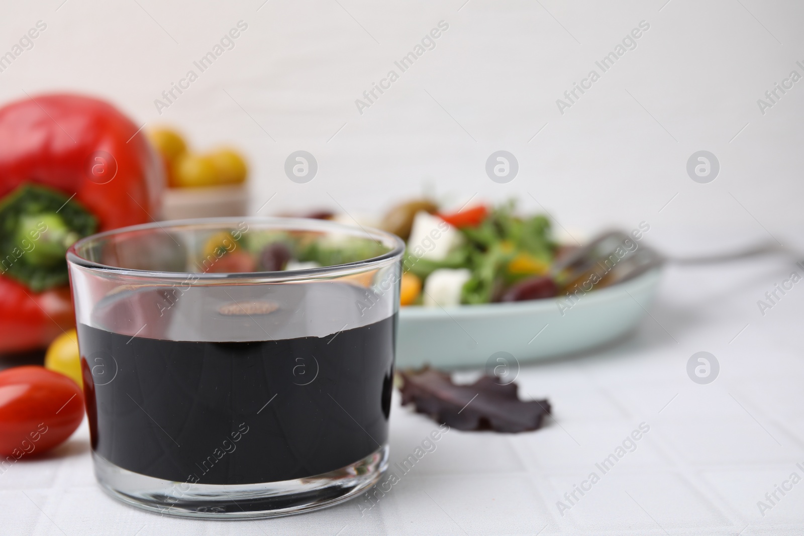 Photo of Vinegar in glass on white tiled table, closeup. Space for text