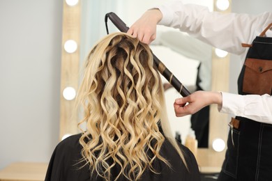 Photo of Hair styling. Hairdresser curling woman's hair in salon, closeup