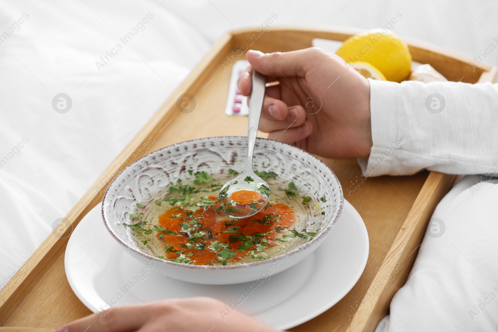 Photo of Sick young man eating soup to cure flu in bed at home, closeup