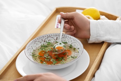 Sick young man eating soup to cure flu in bed at home, closeup